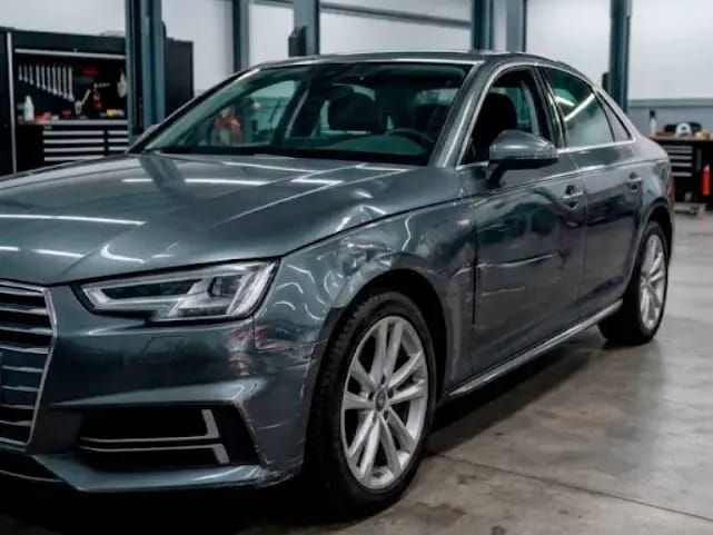 Lateral delantero de un Audi A4 gris con un golpe en la aleta, antes de la reparación de chapa