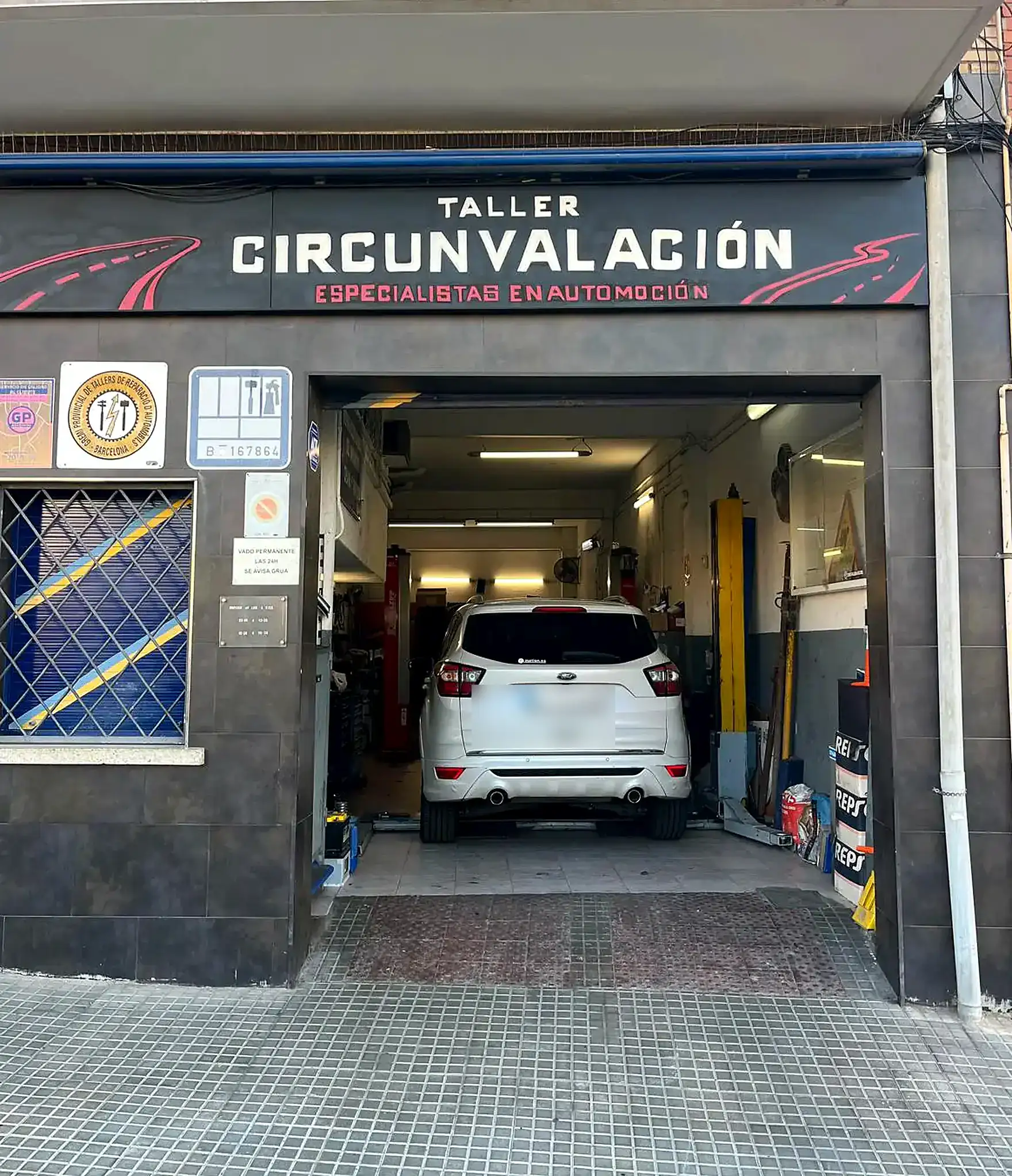 Entrada del Taller Circunvalación en Viladecans, con un vehículo sobre el elevador al fondo